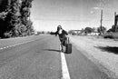 Sister Antonia hitchhiking with a suitcase on a desert road, black and white photograph, 1 May 2016
