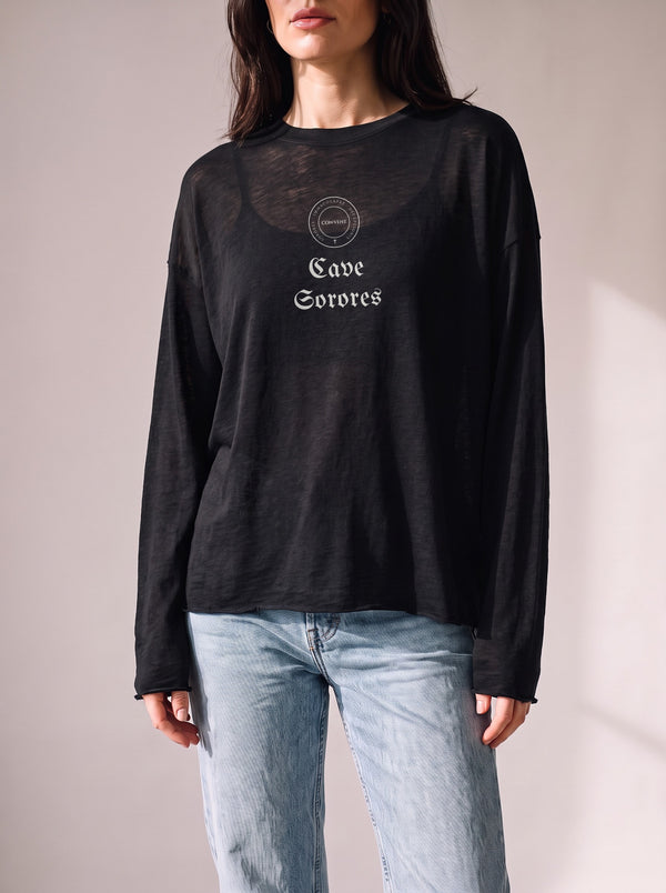 Worn by a woman: Her Sheer Long Sleeve, Cave Sorores on a black sheer raw-edge long sleeve over a black camisole