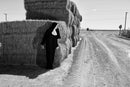 Sister Antonia leaning on hay bales with her hand on her head, a stop sign at the end of the dirt road, black and white photograph, Salton Sea, 1 May 2016